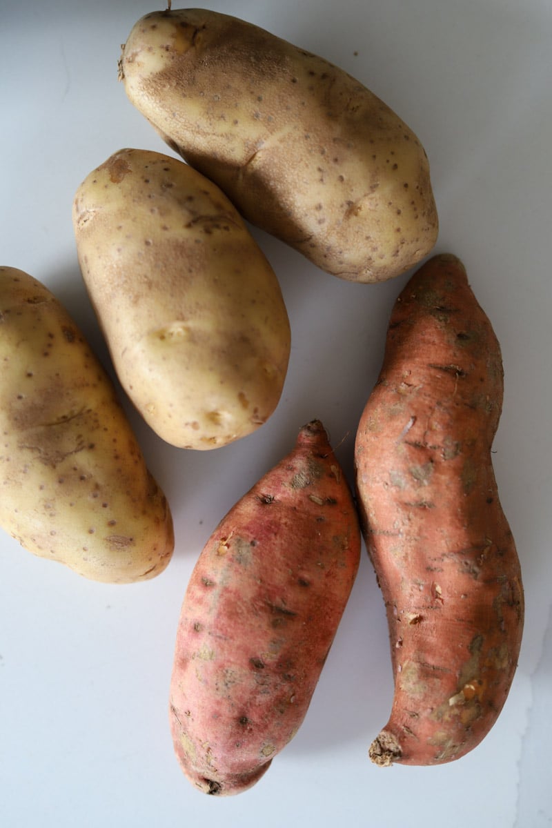 three russet potatoes and two sweet potatoes on a surface