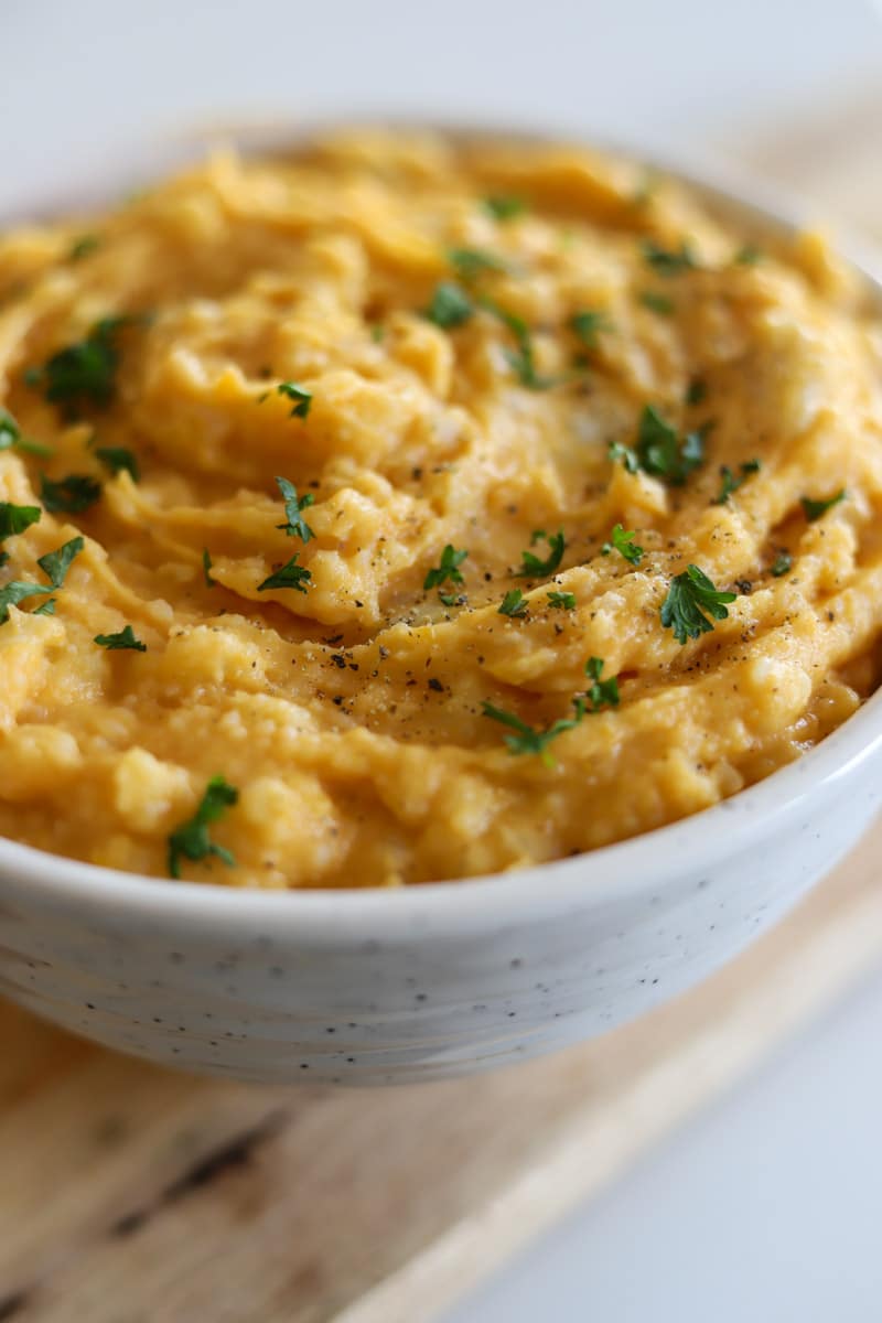 close up bowl of mashed sweet potatoes garnished with fresh parsley