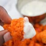 close up view of a hand holding a cauliflower bite dipped in ranch dipping sauce