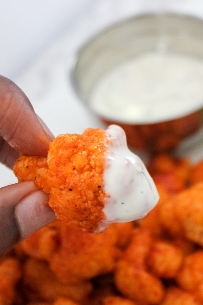 close up view of a hand holding a cauliflower bite dipped in ranch dipping sauce