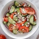 A bowl of Greek salad with cucumbers, tomatoes, red onions, olives, and crumbled feta, lightly tossed in vinaigrette.