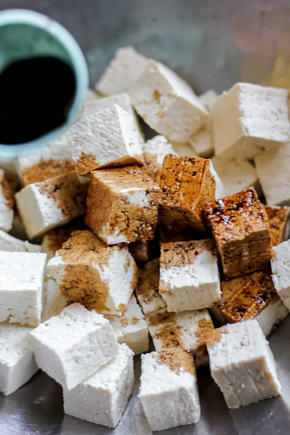 : Firm tofu cubes soaking up soy sauce marinade before cooking.
