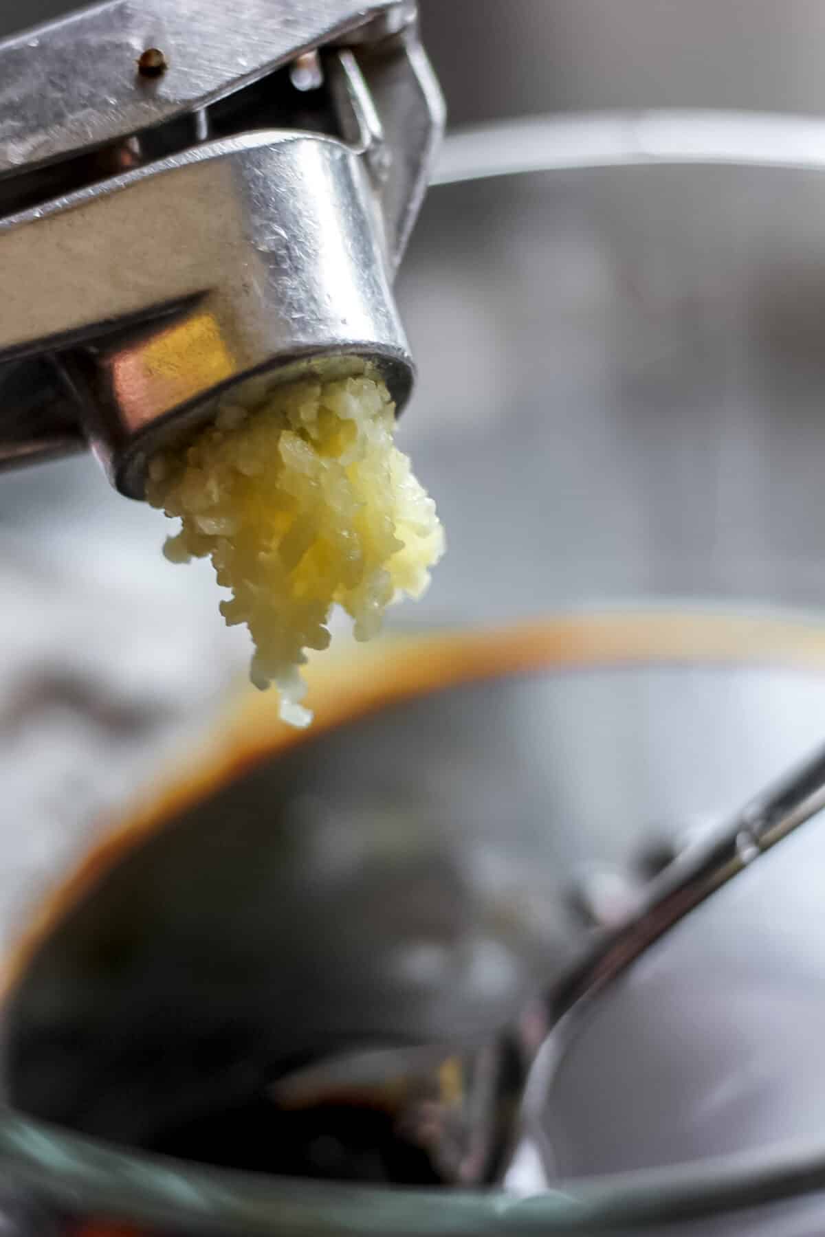 Minced garlic being pressed into a bowl with soy sauce for a flavorful tofu stir-fry sauce.