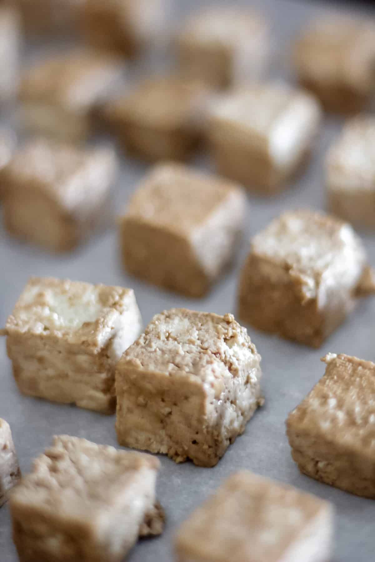 Seasoned tofu cubes spread on a baking sheet, ready to be baked for a crispy texture.