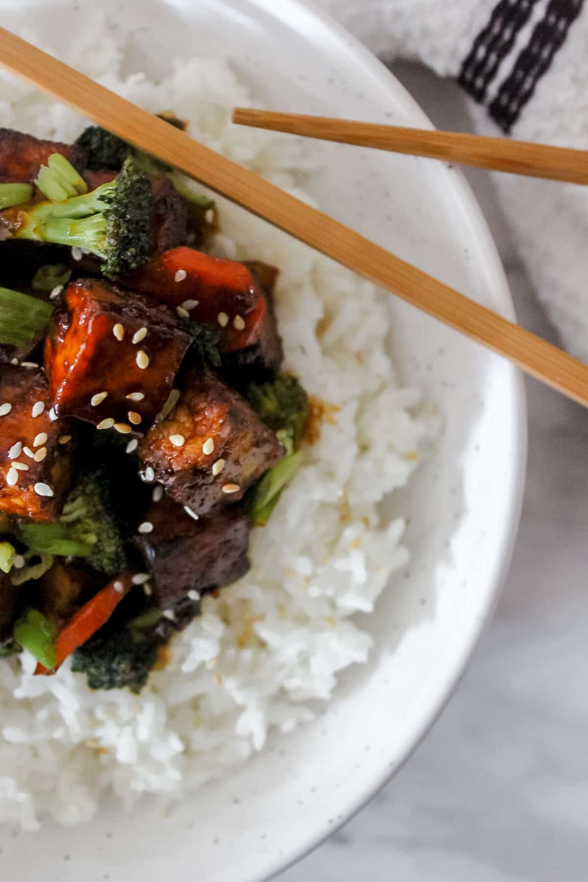 A top-down view of tofu stir fry with broccoli, carrots, and bell peppers served with rice.