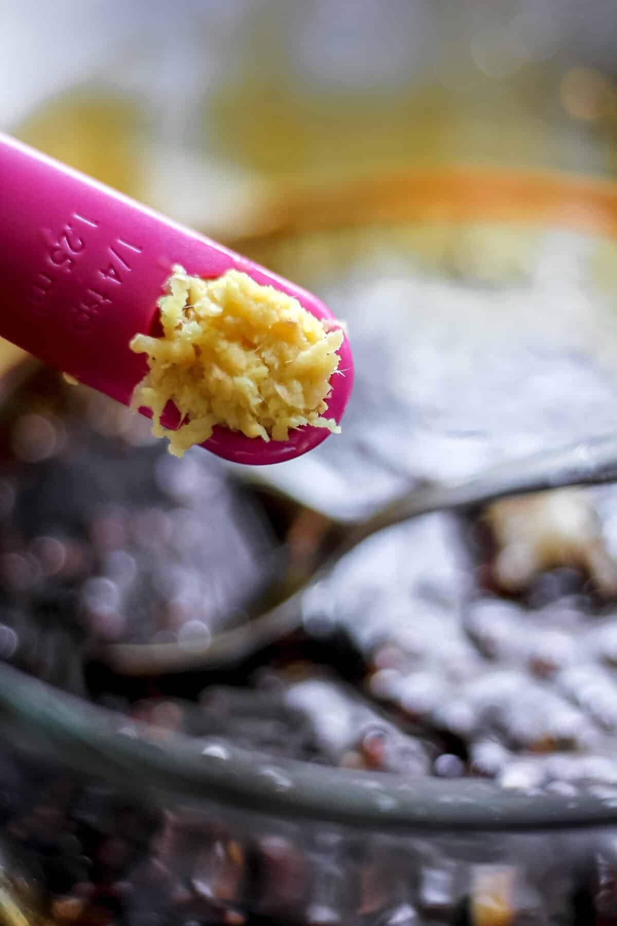 A measuring spoon filled with freshly grated ginger held over a bowl of soy sauce and other ingredients, ready to be mixed into the stir-fry sauce.