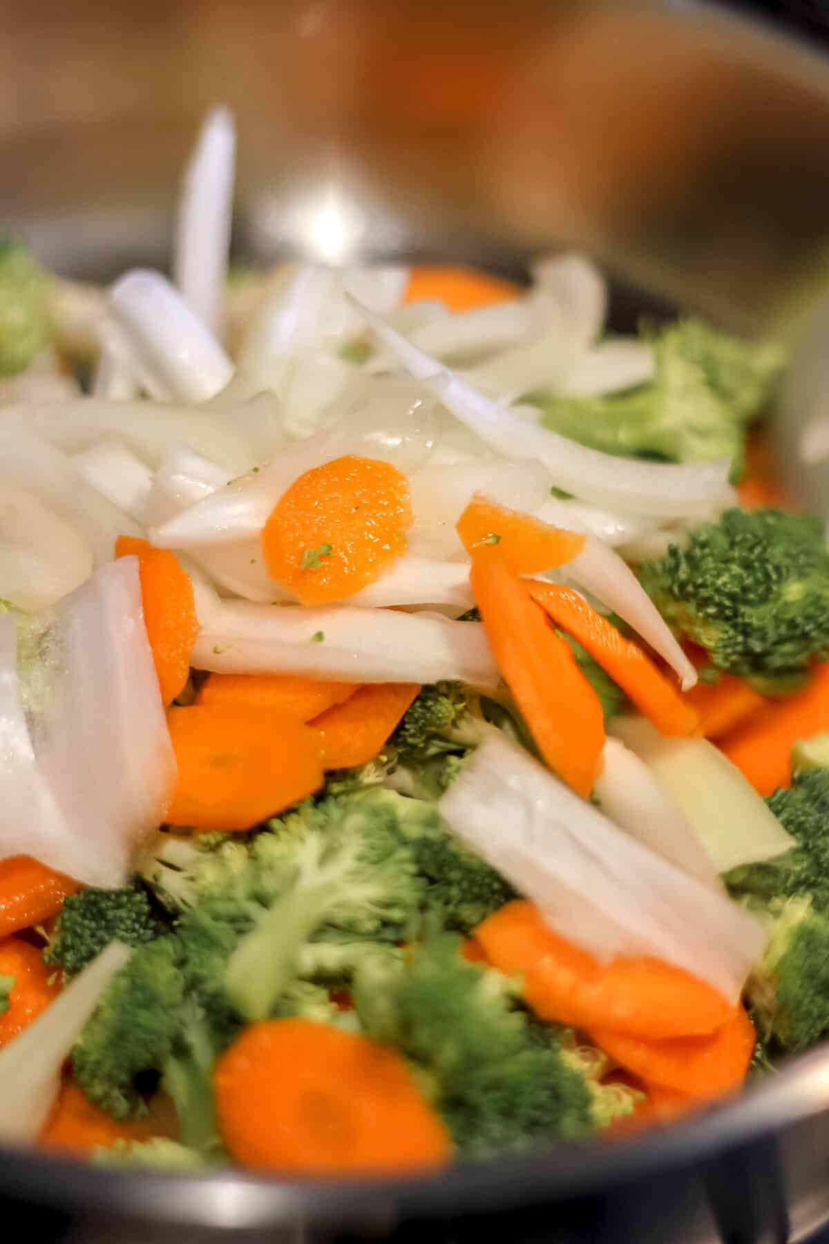 Thinly sliced carrots, onions, and broccoli in a pan, ready for stir-frying.
