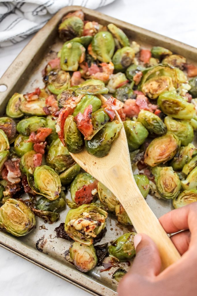 brussels sprouts and bacon on wooden spoon with sheet pan of more brussels and bacon in back