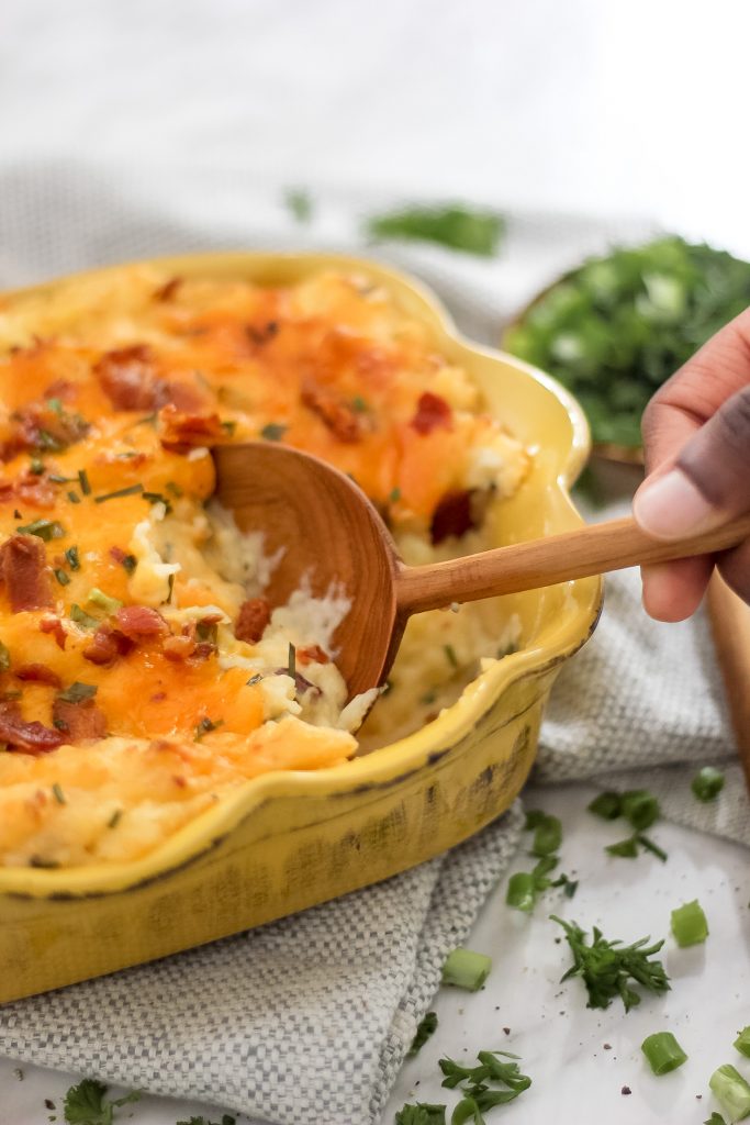 wooden spoon scooping out loaded mash potatoes in yellow casserole dish