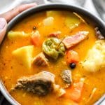 Traditional Jamaican Pumpkin Beef Soup in Bowl with Hand