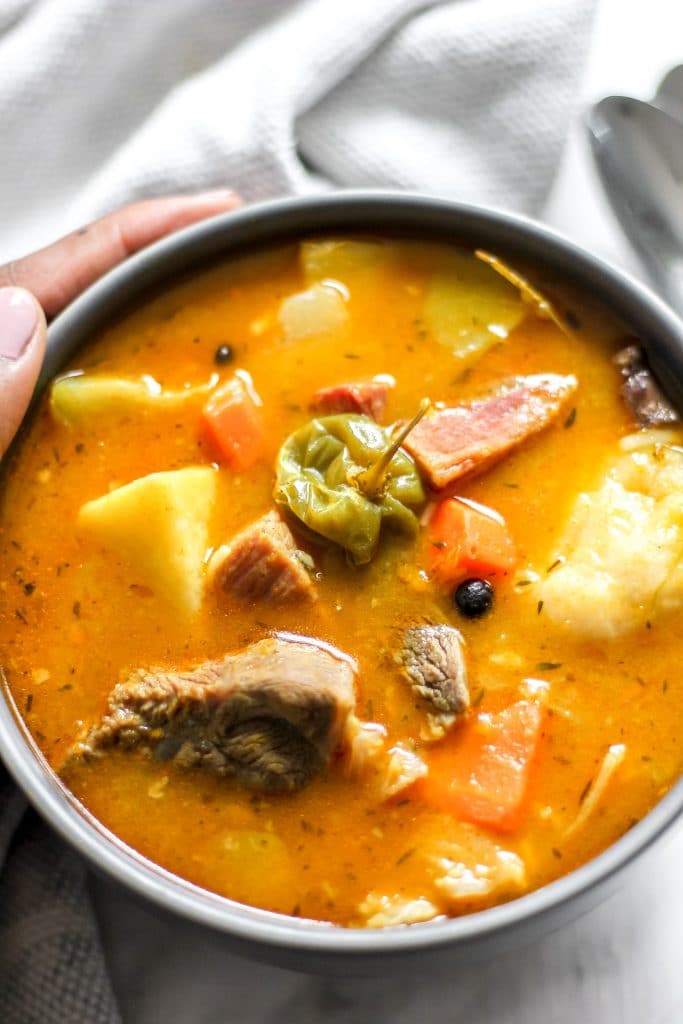 Traditional Jamaican Pumpkin Beef Soup in Bowl with Hand