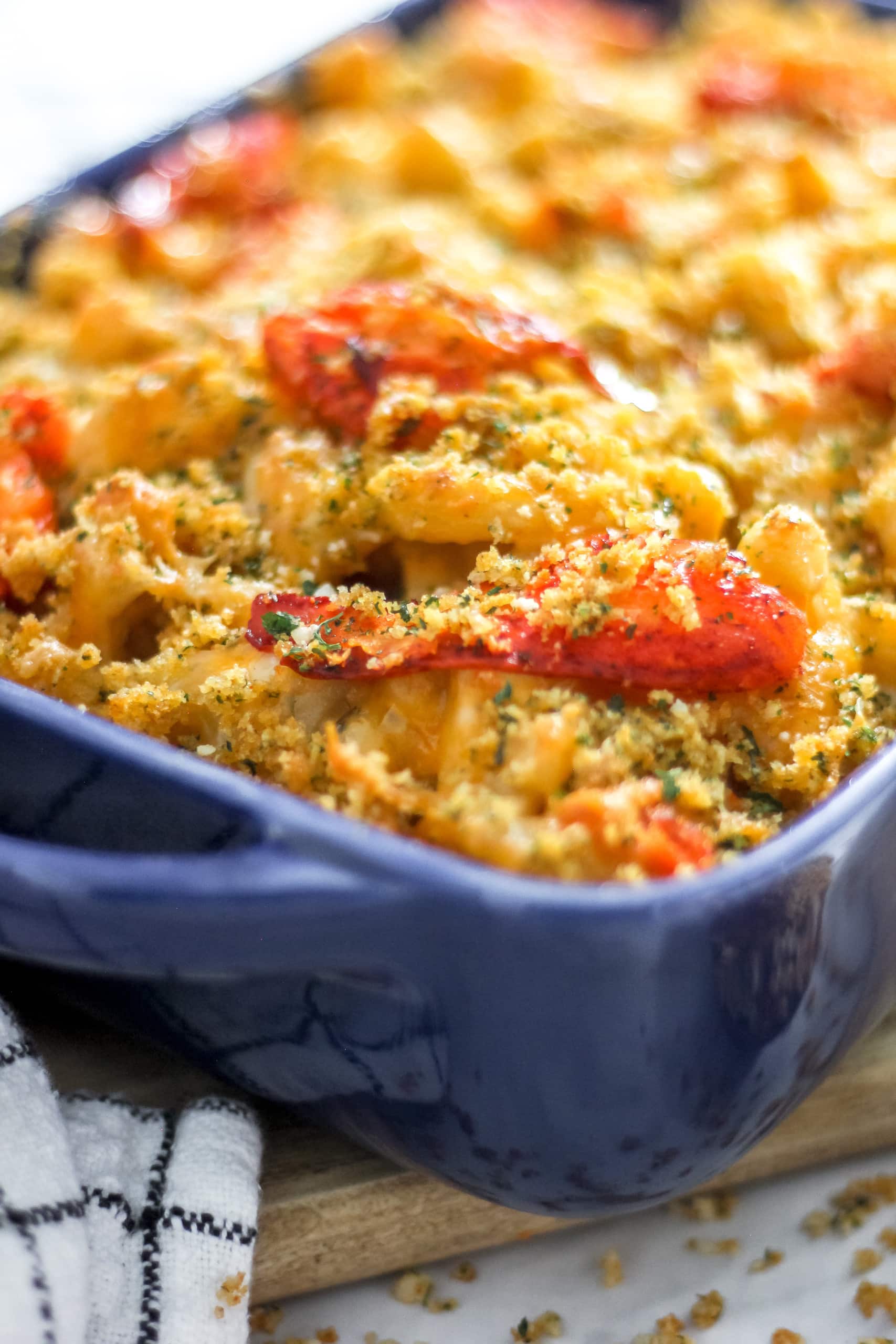 Ultimate Lobster Mac and Cheese in blue casserole dish on wooden plank