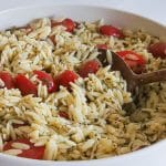 pesto orzo salad with tomatoes in bowl with wooden spoon.