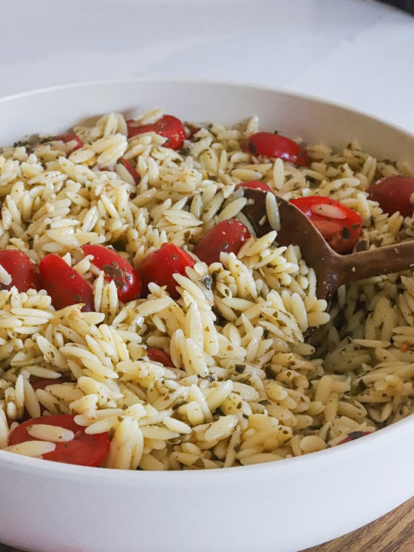 pesto orzo salad with tomatoes in bowl with wooden spoon.