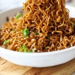 garlic chili oil noodles on chopsticks with sesame seeds and green onions.