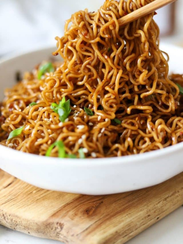 garlic chili oil noodles on chopsticks with sesame seeds and green onions.