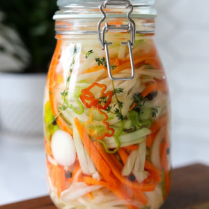 jamaican pickled vegetables (escovitch dressing) in glass jar on wooden board.
