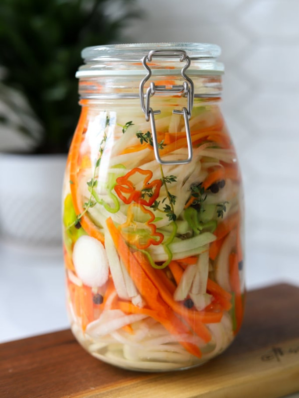 jamaican pickled vegetables (escovitch dressing) in glass jar on wooden board.