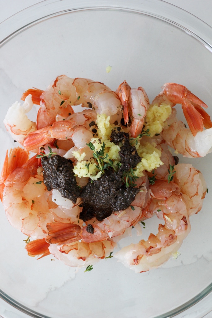 raw shrimp with garlic, thyme, jerk marinade in glass bowl.