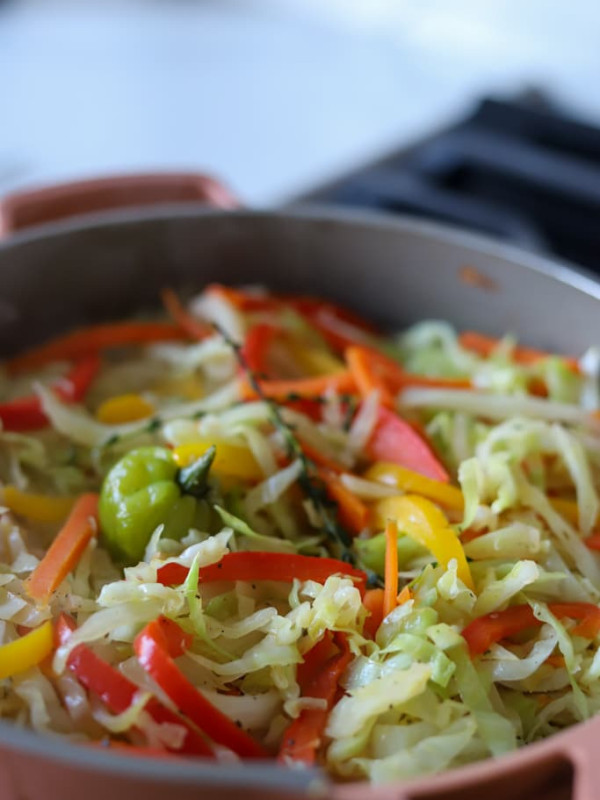 jamaican steamed cabbage with colourful veggies in a coral coloured pan.