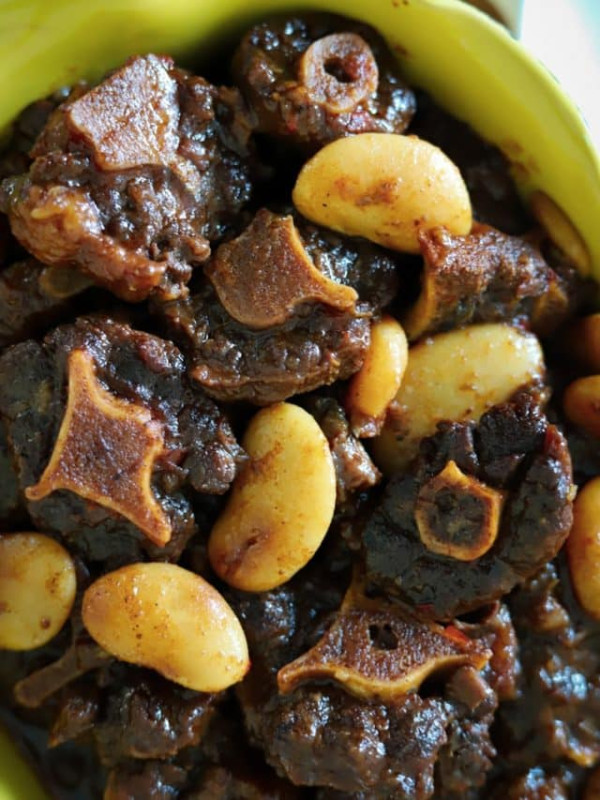 jamaican oxtail with butterbeans in yellow serving dish.