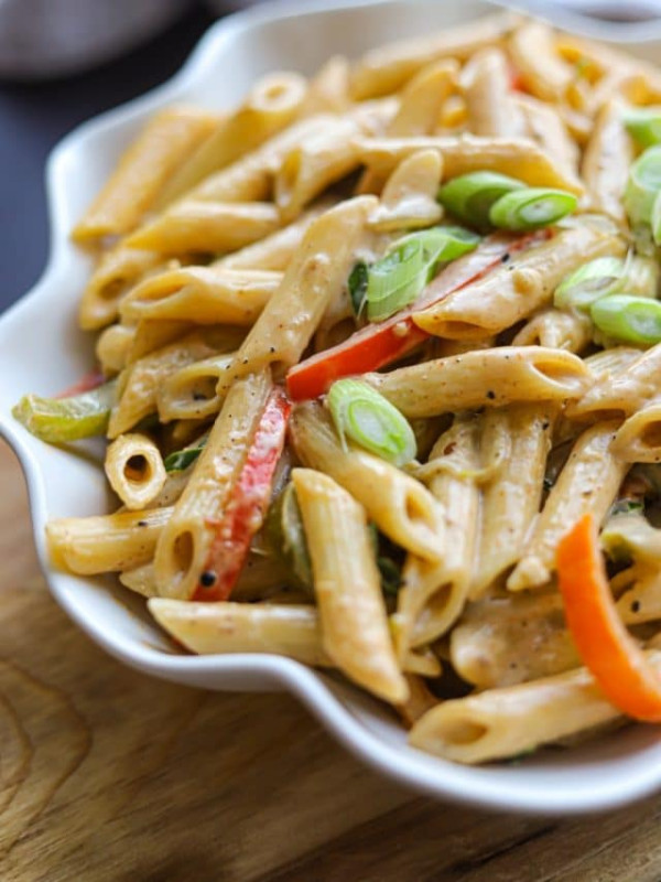 rasta pasta in a white bowl on a wooden plank.