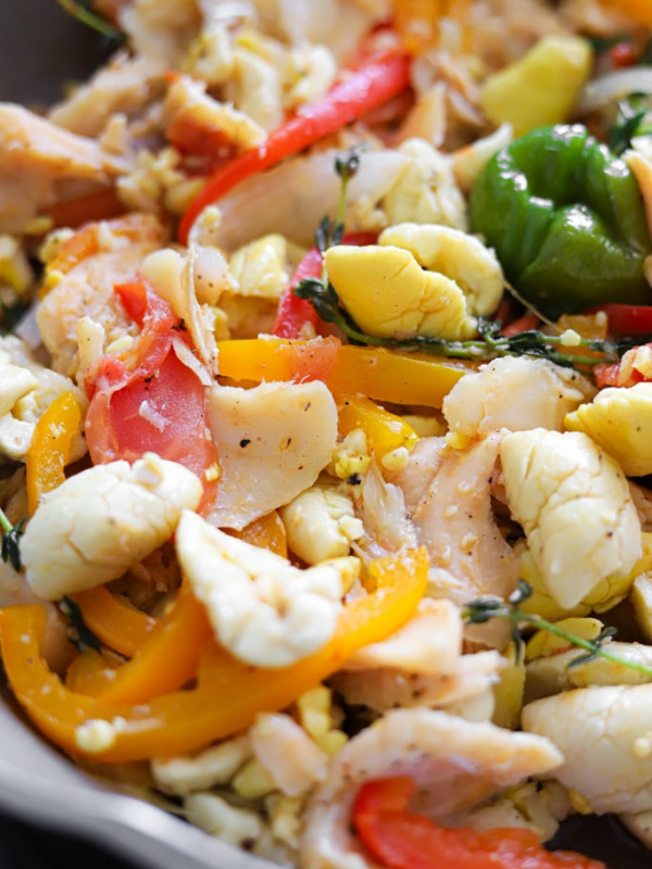 Close-up of cooked ackee and saltfish with colourful bell peppers and thyme sprigs.