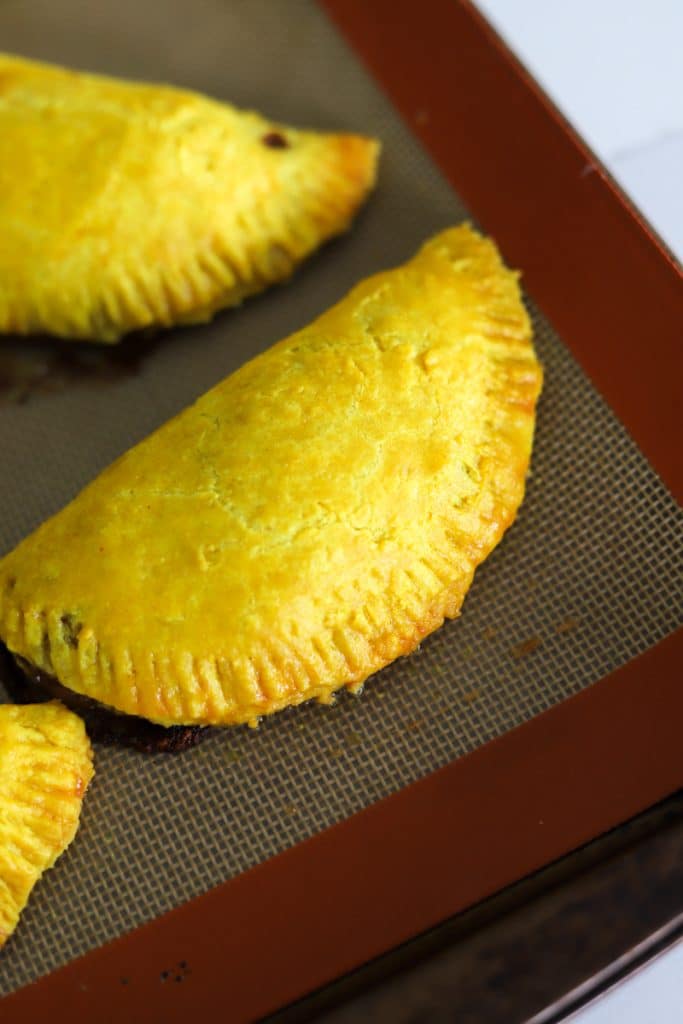 baked jamaican patty resting on baking sheet.