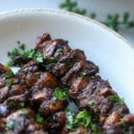 jerk chicken skewers with herb garnish on white plate.