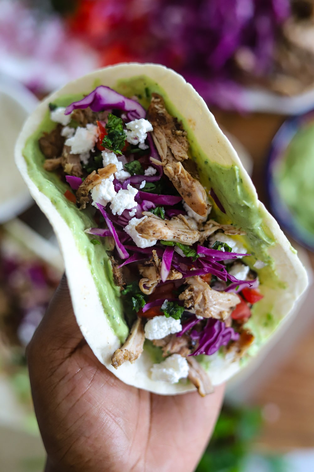 Hand holding soft shell Jamaican jerk chicken taco with avocado crema
