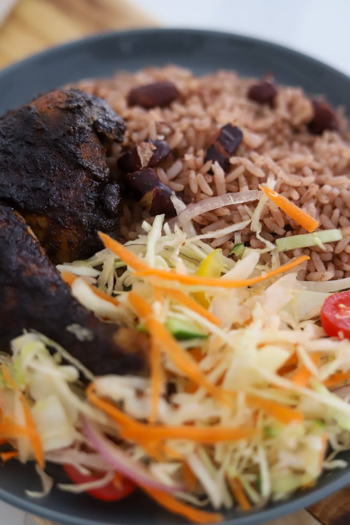 jerk chicken served with rice and peas and coleslaw on plate.