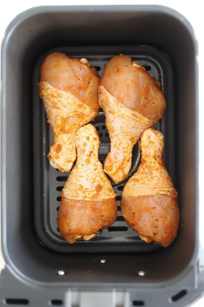 seasoned chicken legs in air fryer basket.