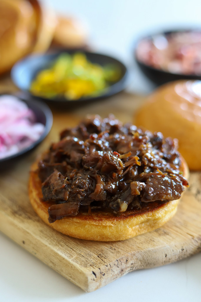 how to make an oxtail sandwich: toasted brioche bun with oxtail meats on top.