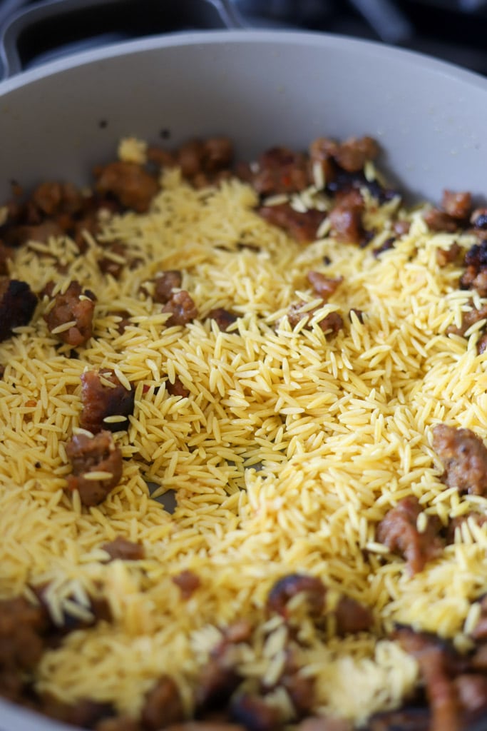 toasting orzo in skillet with sausage.