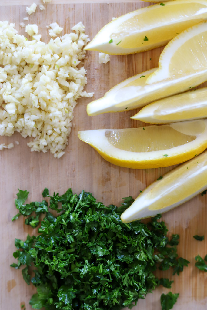 minced garlic, fresh parsley, and lemon wedges on cutting board.