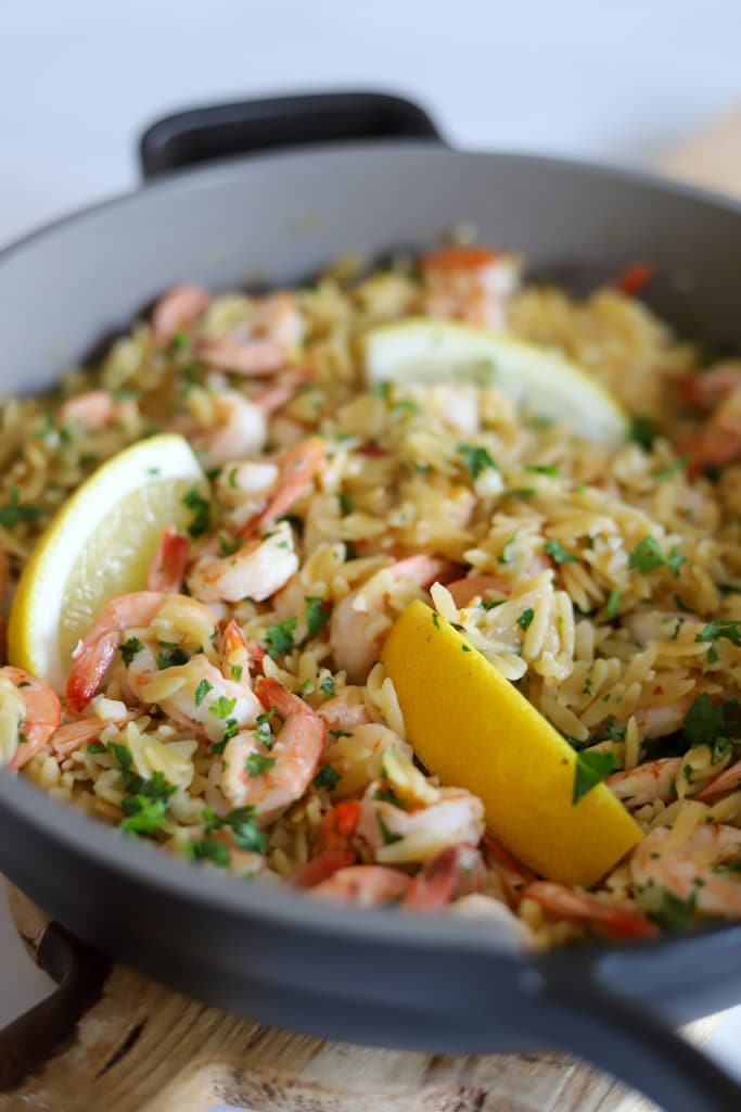 shrimp orzo in skillet with lemon wedges and fresh parsley garnish.