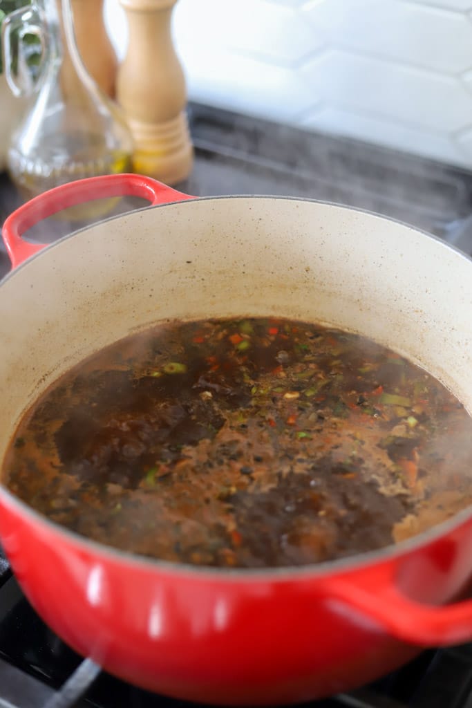 vegetables and aromatics with beef broth simmering in pot.