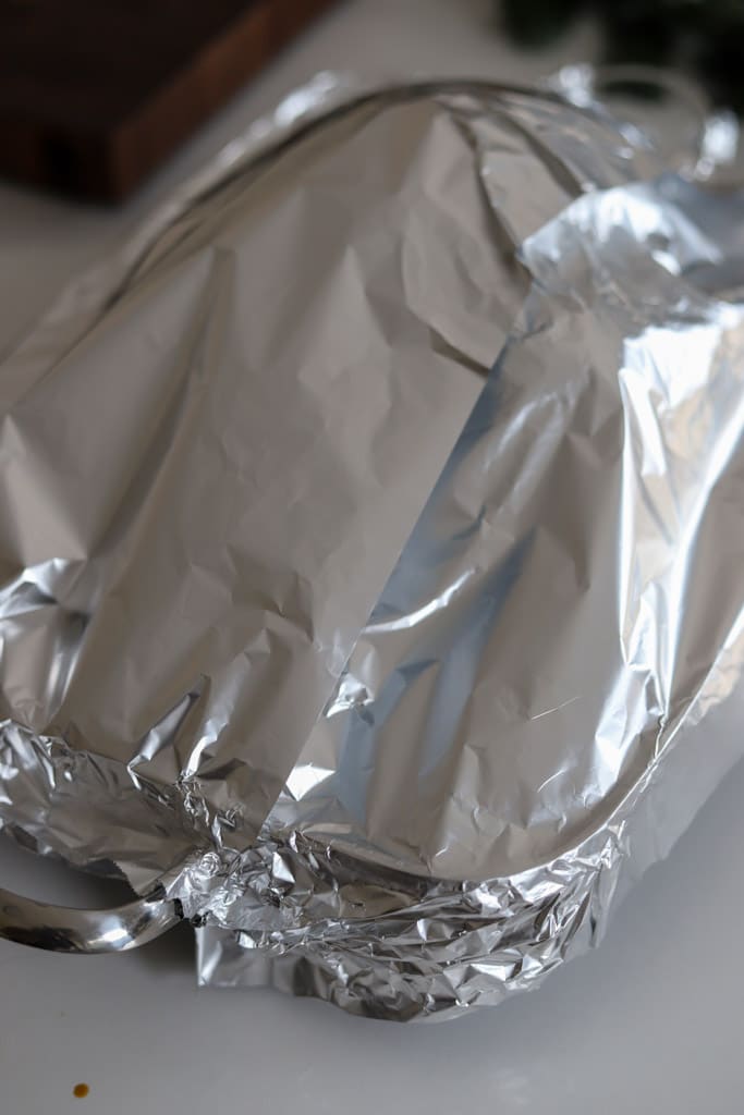 a whole turkey covered in foil before roasting