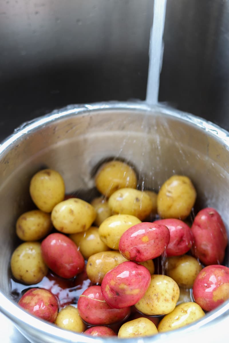 gold and red baby potatoes in a large pot with water being poured into it