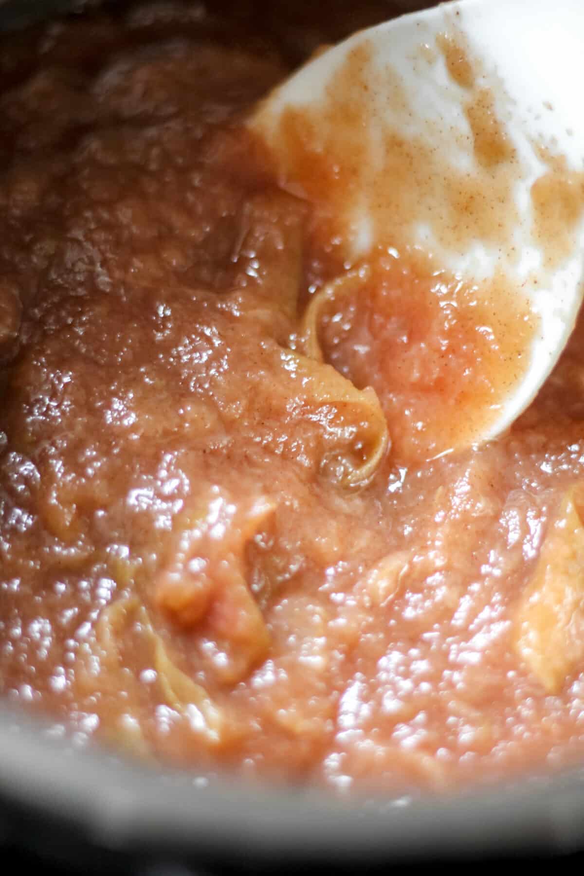 Cooked apple mixture being stirred inside the Instant Pot with a white spatula.