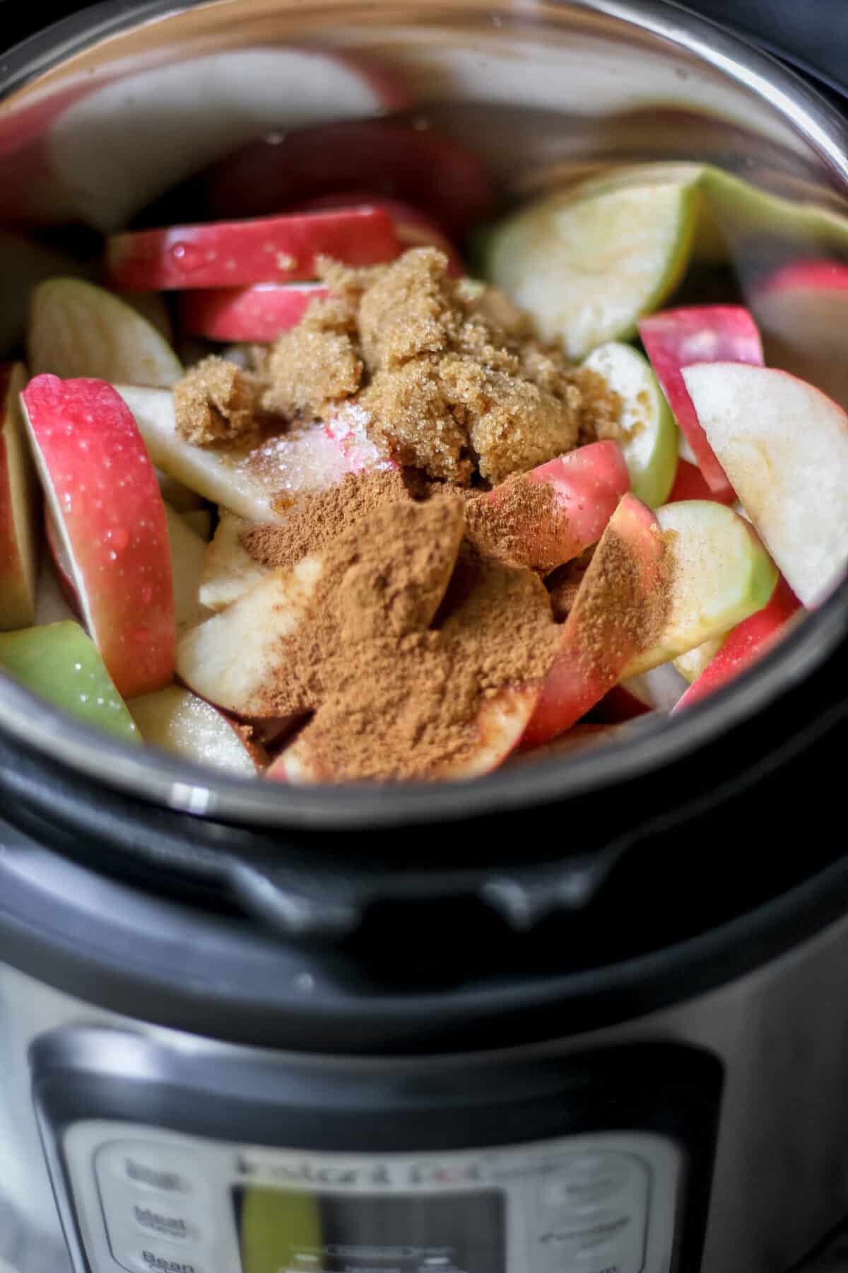 Sliced apples in an Instant Pot topped with brown sugar and ground spices before cooking.