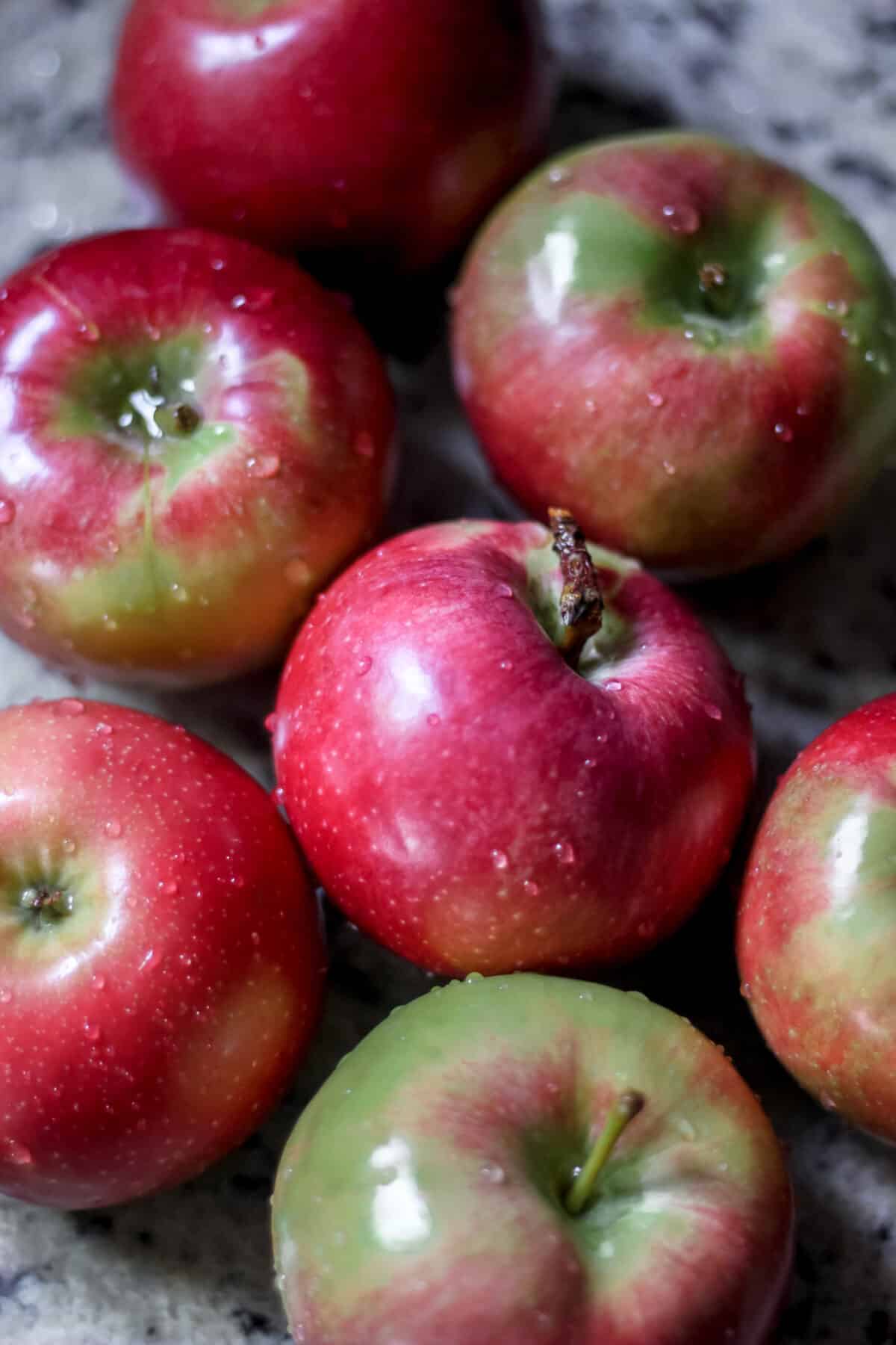 Fresh red and green apples with water droplets on a countertop.
