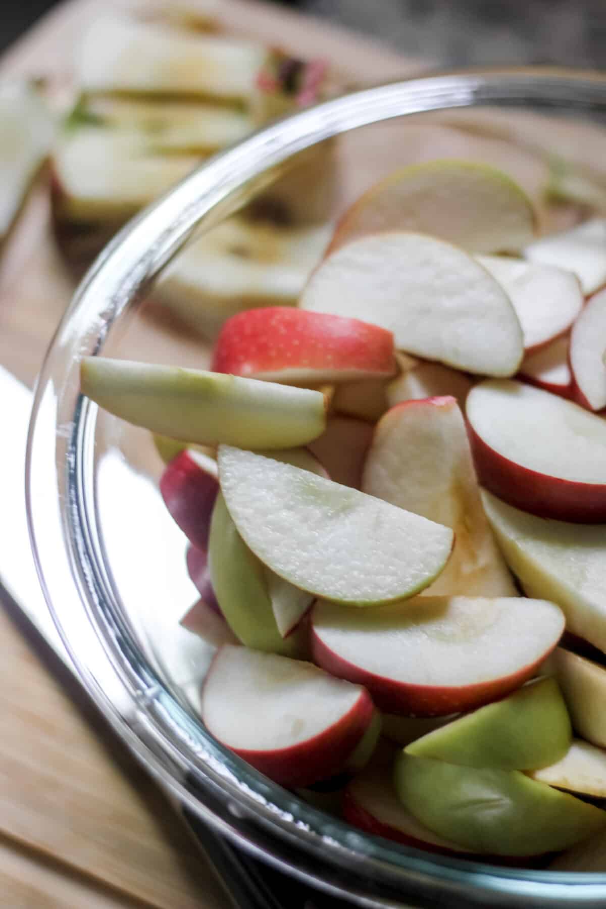 A glass bowl filled with freshly sliced apple wedges on a cutting board.