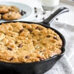 Close-up of a cast iron skillet filled with sea salt chocolate chip cookie, resting on a grey kitchen towel.