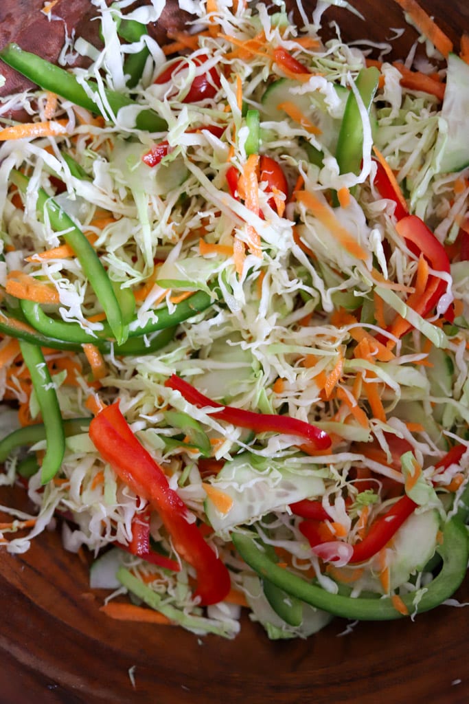 Bowl of shredded cabbage, carrots, cucumbers, and red and green bell peppers mixed together.