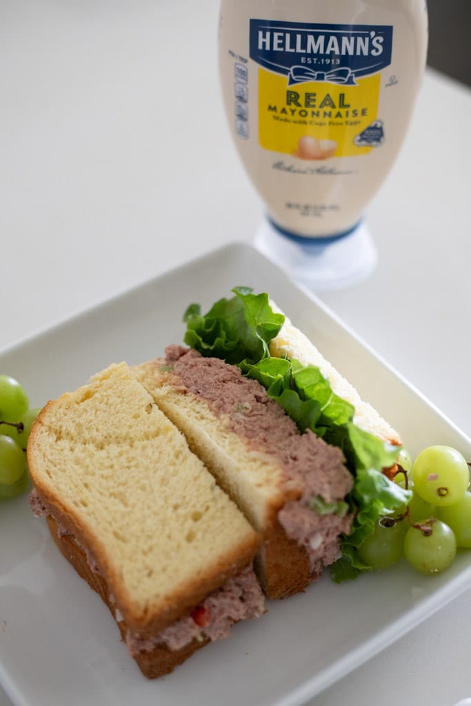 Half of a corned beef sandwich with lettuce on a plate beside green grapes.