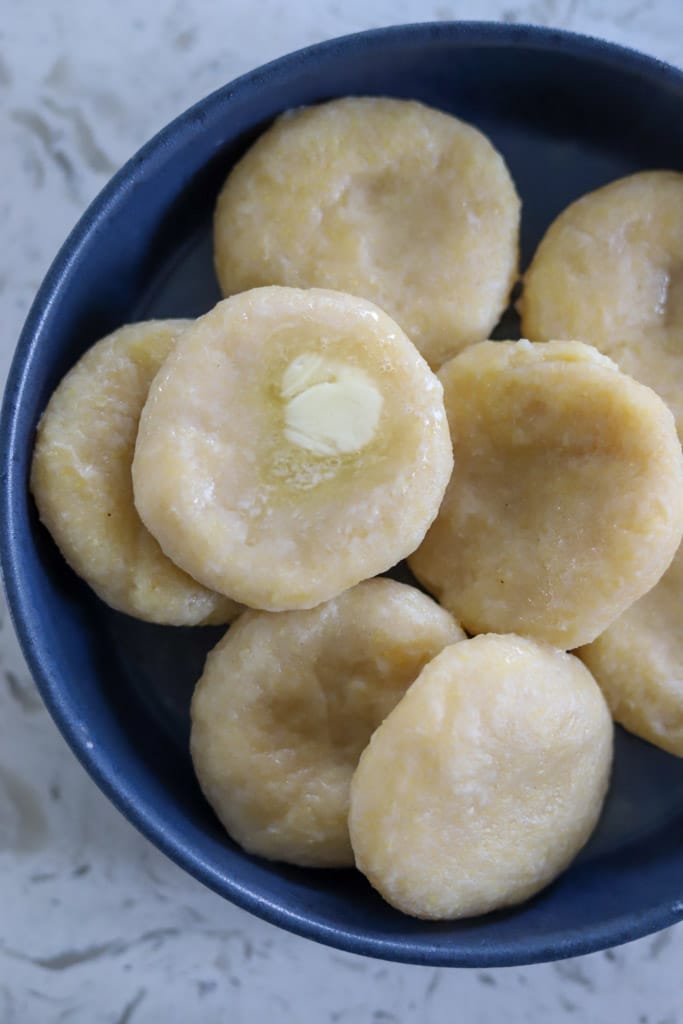 Formed cornmeal dumplings shaped into discs on a blue plate.