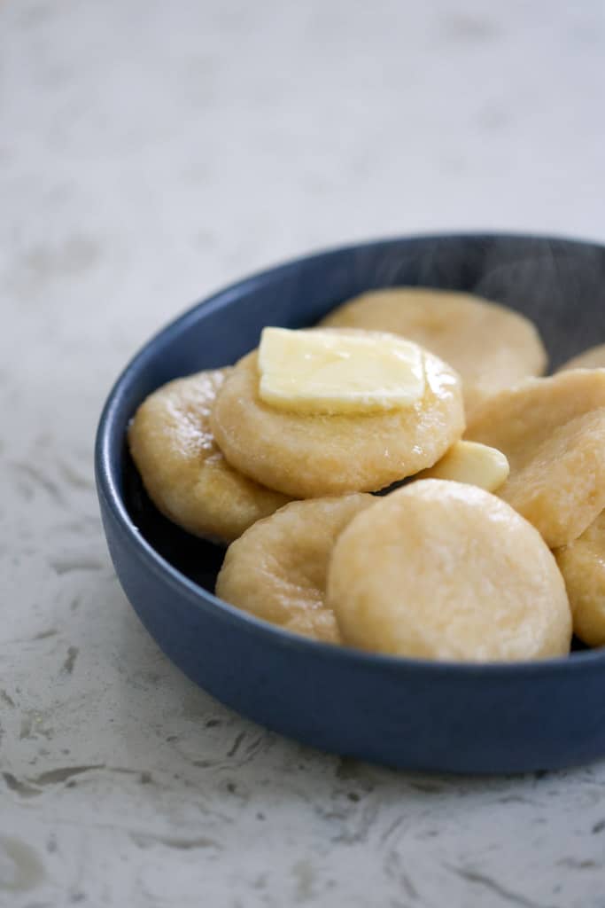 Blue bowl filled with dumplings, topped with a pat of butter.