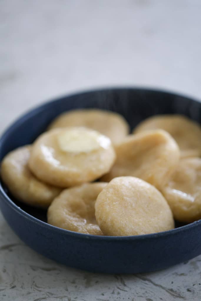 Blue bowl of dumplings glistening with butter on top.
