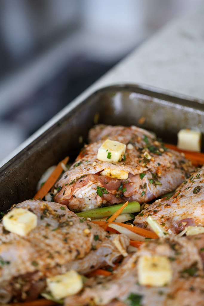 Turkey thighs in a roasting pan with butter pieces and vegetables underneath.